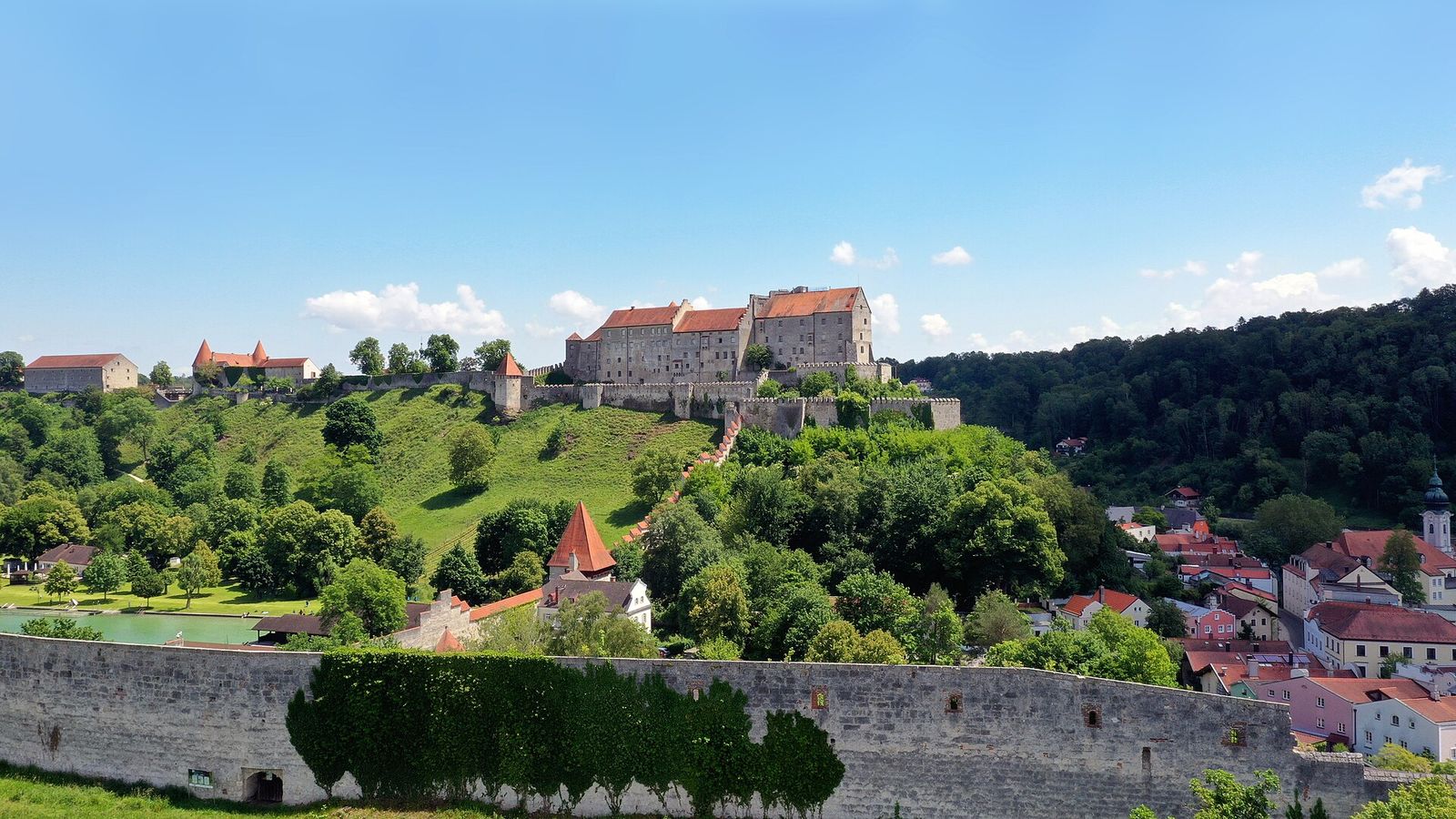 Die langgestreckte Burg zu Burghausen auf dem Höhenrücken über der Altstadt, im Vordergrund eine alte Bruchsteinmauer