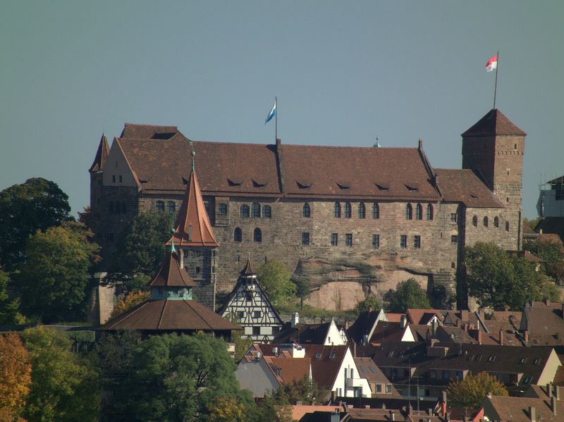 Die Kaiserburg Nürnberg aus Sandstein auf ihrem Felsen, davor Dächer und ein Fachwerkgiebel der Altstadt