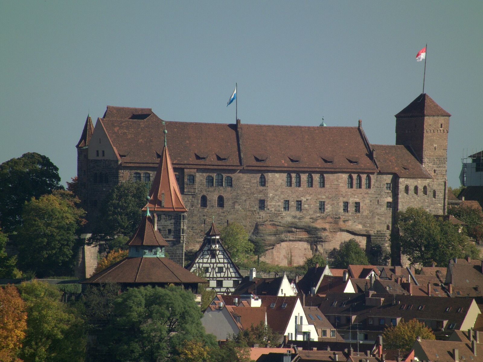 Die Kaiserburg Nürnberg aus Sandstein auf ihrem Felsen, davor Dächer und ein Fachwerkgiebel der Altstadt