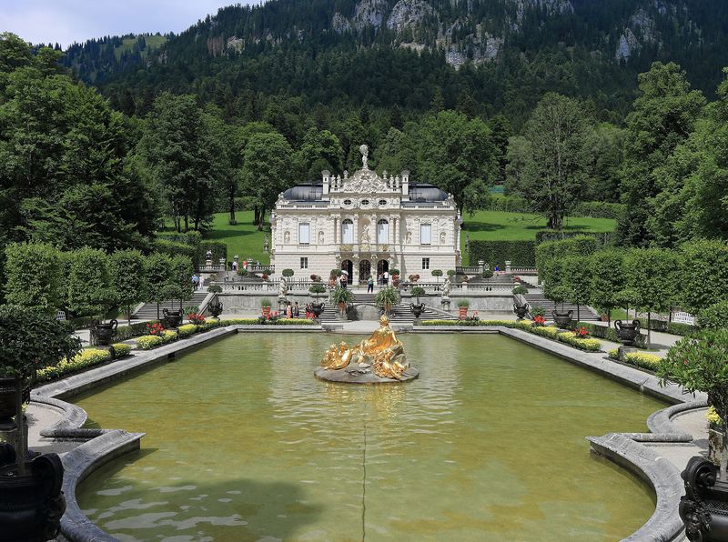Schloss Linderhof hinter dem Wasserbecken mit vergoldeter Brunnenfigur, umgeben von Gartenterrassen und bewaldeten Berghängen