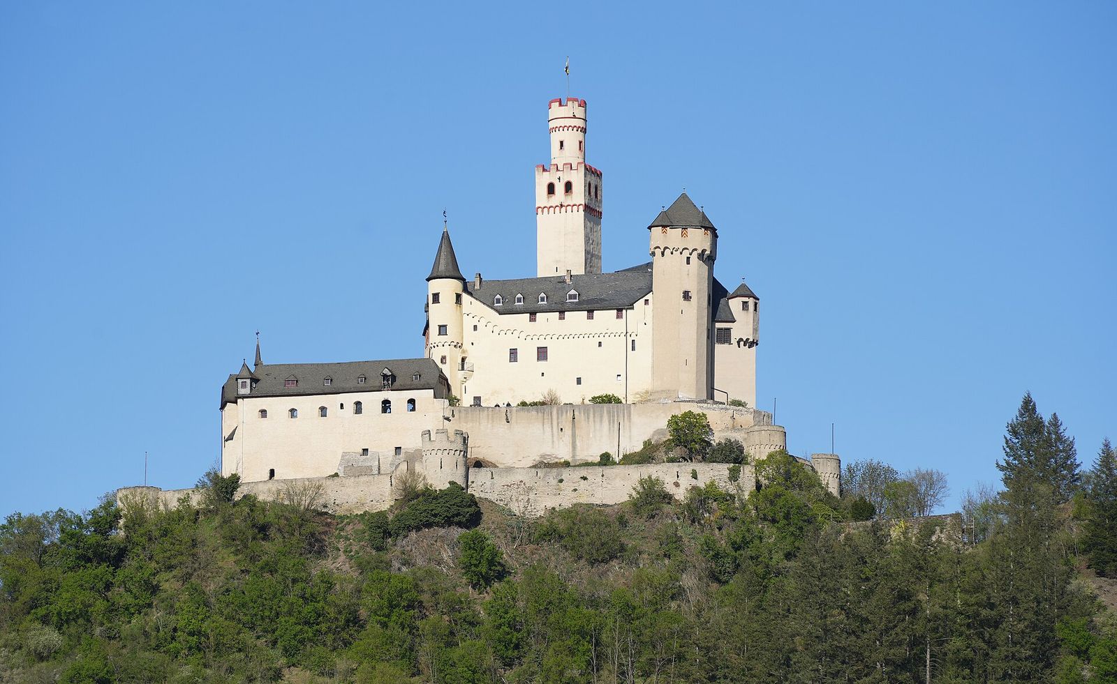 Die helle Marksburg mit hohem Bergfried auf einer bewaldeten Kuppe über dem Rhein bei Braubach