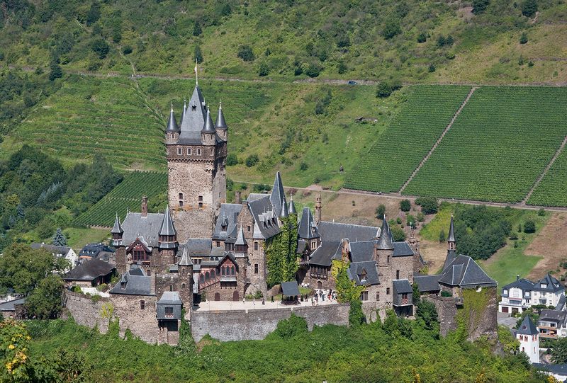 Die Reichsburg Cochem mit Bergfried und spitzen Türmchen, im Hintergrund steile Weinbergterrassen